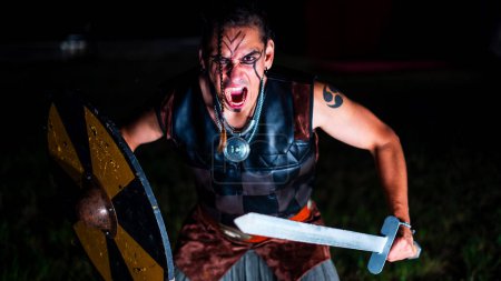 Photo for Viking warrior shouting during battle with black war paint, openig his mouth and holding his sword. - Royalty Free Image