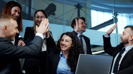 Photo for Business people in official wear gathering together in office in front of laptop, watching online trading, feeling happy and giving high five. Successful team - Royalty Free Image