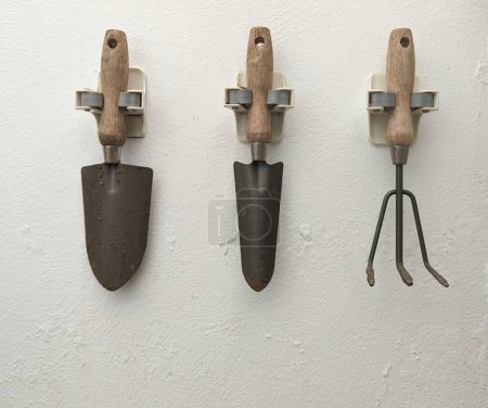 Used gardening elements, two shovels and one rake, with wooden handle, placed on white wall, centered