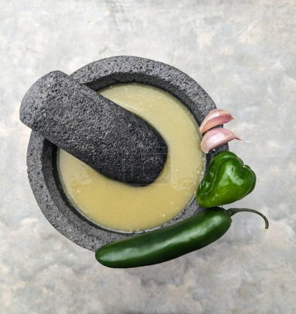 Foto de Mortero y mortero de piedra, salsa verde mexicana, dientes de ajo, habanero y chiles jalapeños sobre fondo de cemento - Imagen libre de derechos