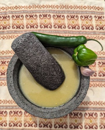 Foto de Mortero y mortero de piedra, salsa verde mexicana, ajo, habanero y chiles jalapeños mantel mexicano hecho a mano - Imagen libre de derechos