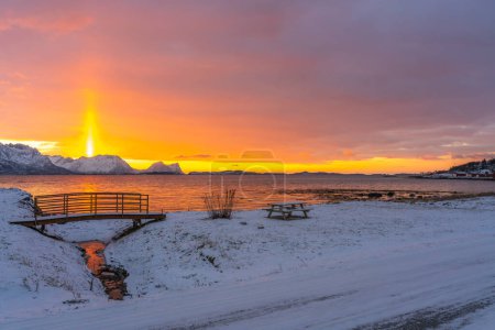 Foto de Farbiger Sonnenuntergang mit Lichtstrahl ber den Bergen von Senja mit einer Brcke im Vordergrund, am Strand des Bergfjorden auf Senja, Norwegen. - Imagen libre de derechos