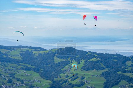Foto de Paisaje alpino con volantes de paracaídas en cielo azul nublado, alto sobre prado verde, abeto, lago Constanza con agua azul y cordillera. día de verano en los Alpes del bosque de Bregenz, Vorarlberg, - Imagen libre de derechos