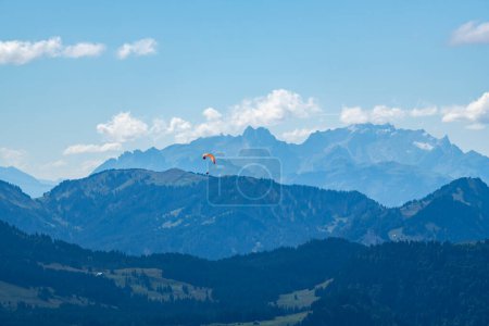 Foto de Paisaje alpino con volantes de paracaídas en cielo azul nublado, alto sobre prado verde, abeto y cordillera suiza. día de verano en los Alpes del bosque de Bregenz, Vorarlberg, - Imagen libre de derechos