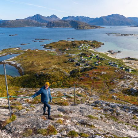 Wanderin in der herbstlichen Natur Norwegens. Wandern am Fjord und in den Bergen auf der Insel Kvalya in Troms, zwischen grünen, orangen und roten Pflanzen. Wanderer auf dem Weg, Wanderparadies rund um Sommarya
