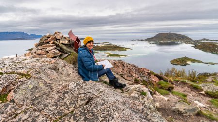Wanderin in der herbstlichen Natur Norwegens. Wandern am Fjord und in den Bergen auf der Insel Kvalya in Troms, zwischen grünen, orangen und roten Pflanzen. Wanderer auf dem Weg, Wanderparadies rund um Sommarya
