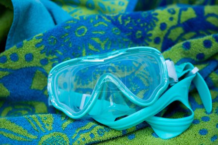 Photo for Blue swimming googles resting on blue and green beach towel, near the pool - Royalty Free Image