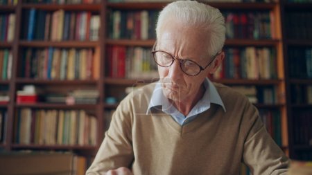 Foto de Mature gray-haired librarian in eyeglasses reading a book or checking logbooks in the library - Imagen libre de derechos