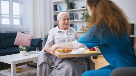 Photo for Retirement home nurse bringing meal to a senior woman, taking care of a tenant - Royalty Free Image