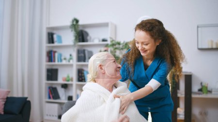 Pflegende Krankenschwester bringt Decke zum Aufwärmen der Seniorin in Altenheim