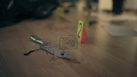 Foto de Primer plano de un cuchillo ensangrentado con un marcador de escena del crimen en el suelo, que sirve como arma homicida y evidencia crucial - Imagen libre de derechos