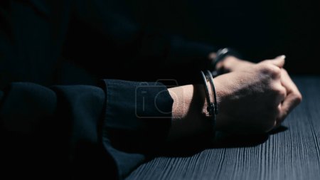 Photo for Female hands in handcuffs are leaning on a table in an interrogation room, close-up - Royalty Free Image