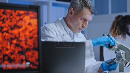 Photo for Scientist adjusting microscope to examine blood sample, diagnostics and treatment - Royalty Free Image