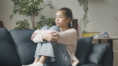 Photo for Sad African American girl sitting on couch alone, teenager suffering loneliness - Royalty Free Image