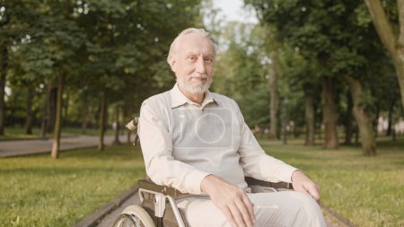 Foto de Hombre satisfecho en silla de ruedas sonriendo a la cámara, descansando en el parque, hogar de ancianos - Imagen libre de derechos