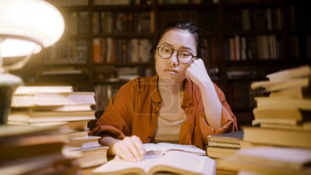 Photo for Portrait of sad female asian student studying late at library, tired freelancer - Royalty Free Image
