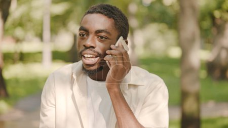 Téléchargez les photos : Homme noir stressé parler au téléphone dans le parc, résoudre des problèmes de travail ou de famille - en image libre de droit