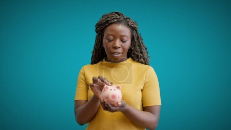 Photo for Young African woman putting coin in piggybank, planning budget, investment - Royalty Free Image