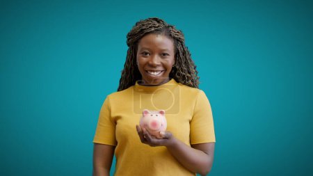 Photo for Smiling African American woman holding piggy bank in hand, saving money, budget - Royalty Free Image