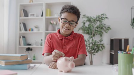 Photo for Smiling black boy putting coin in piggybank, financial literacy for kids, money - Royalty Free Image
