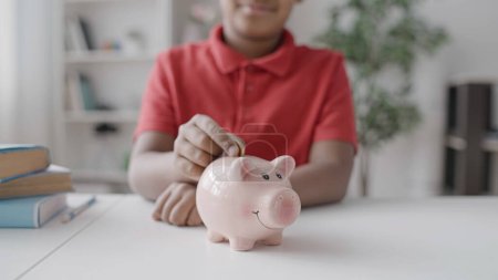 Photo for School kid saving money, putting coin in piggybank on the table, financial plan - Royalty Free Image