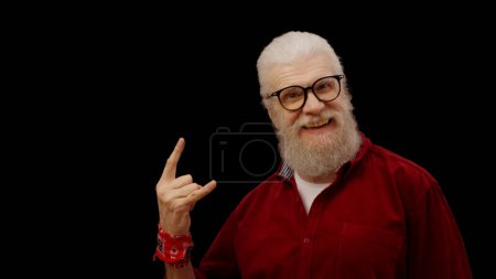 Téléchargez les photos : Contemporary grandpa shows hand horns on camera, representing the spirit of forever young and a rockstar - en image libre de droit