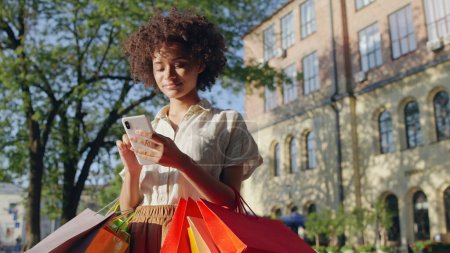 Jeune femme souriante choisir des vêtements en ligne dans l'application smartphone, achats mobiles