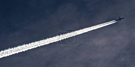 Transport airplane makes the very strong trace line of chemtrails on blue sky. Conspiracy theory.