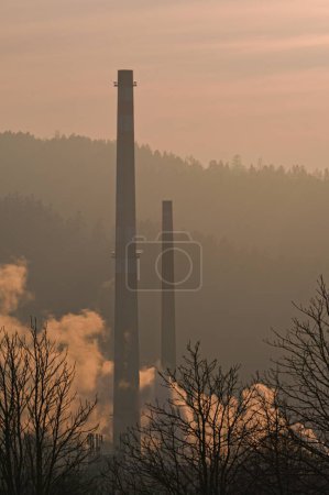 Téléchargez les photos : Vieille cheminée haute dans la zone industrielle et atmosphère brumeuse coucher de soleil sur le fond. Roznov pod Radhostem, République tchèque. - en image libre de droit