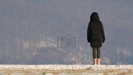Téléchargez les photos : Une jeune fille solitaire à l'horizon regarde la vallée. L'hiver. Paysage couvert de neige. Espace de copie. - en image libre de droit