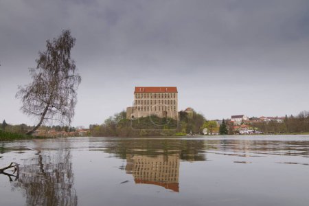 Die historische Burg Plumlov aus dem 17. Jahrhundert und die Reflexion auf der Oberfläche des Teiches im Bezirk Prostejov in der Tschechischen Republik. Bewölkter Rauch nebelt Luftverschmutzung ein.