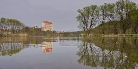 Historical Plumlov castle from 17th century and reflection on the surface of the pond in Prostejov district in Czech republic. Cloudy smoke fog air pollution sky.