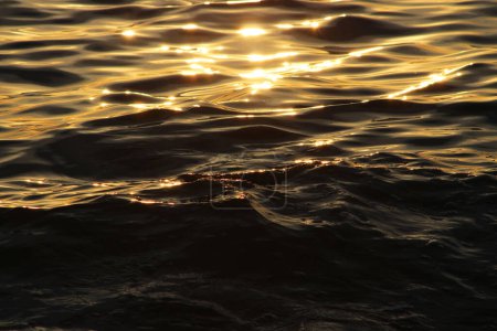 Foto de Atardecer dorado sobre el mar de color naranja brillante, línea amarilla de los últimos rayos de sol, resplandor de sol en el agua oscura calma con poca ondulación de la brisa, textura del agua. - Imagen libre de derechos