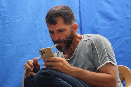 Foto de El hombre pasa tiempo en internet viendo videos en las redes sociales y fumando narguile. Concepto de tiempo libre idea. - Imagen libre de derechos