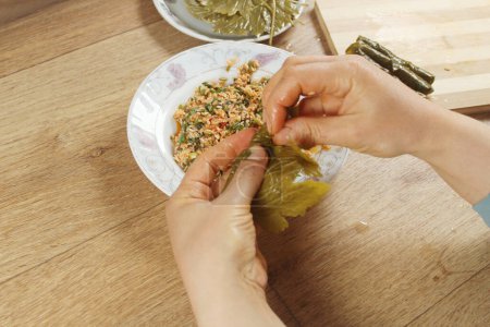 Woman hands preparing wrap stuffed with rice ingredient. Greek or Turkish food Yaprak Sarma or Dolma preparation. Traditional aegean food in Turkey.