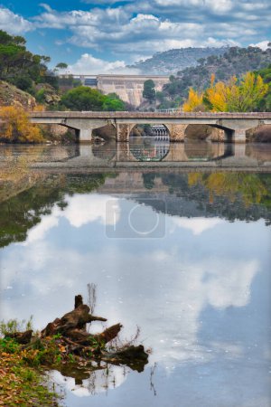 Foto de Aguas tranquilas del río Alberche, con el puente sobre la autopista M-501 y el embalse de San Juan al fondo, en Pelayos de la Presa, Madrid (España)). - Imagen libre de derechos