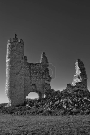 Black and white photograph of the ruins of the castle in the abandoned town of Caudilla, Toledo (Spain), with the figure of a Christ on top of a tower.