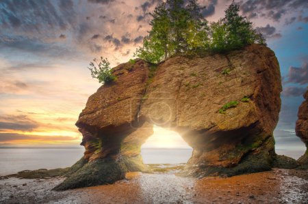 Colourful sunrise sky at low tide, with sun rays through Lovers Arch, Bay of Fundy, Hopewell Rocks Provincial Park, Hopewell Cape, New Brunswick, Canada. 