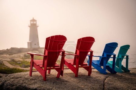 Foto de Cuatro sillas Adirondack frente al faro de Peggys Cove durante la noche nublada al atardecer, Nueva Escocia, Canadá. Foto tomada en septiembre de 2023. - Imagen libre de derechos