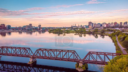 Luftpanorama von der Innenstadt von Ottawa und Gatineau, Chief William Commanda Bridge, nationale Hauptstadtregion, Goldene Stunde Himmel reflektiert über dem Ottawa River, Ontario, Quebec, Kanada September 2021