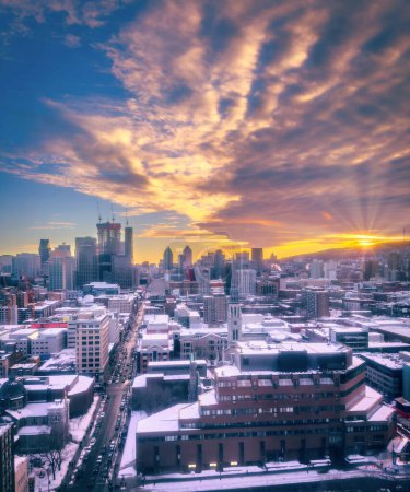 Lila Sonnenuntergänge und bunte Wolken über der Saint-Catherine Street, die Skyline der Innenstadt von Montreal mit Schnee bedeckt, und Strahlen über dem Mount Royal, Quebec, Kanada. Vertikale Winteraufnahme vom Februar 2023