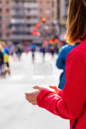 Photo for Blonde woman in a red jacket, clapping at a marathon - Royalty Free Image
