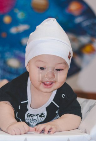 Bebé vistiendo traje negro y sombrero blanco, acostado boca arriba, despierto y mirando a la cámara, con un fondo universal