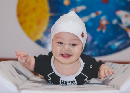 Bebé vistiendo traje negro y sombrero blanco, acostado boca arriba, despierto y mirando a la cámara, con un fondo universal