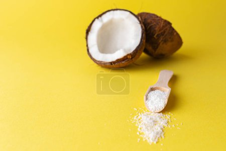 Cuchara de coco y madera con harina de coco sobre fondo de color amarillo. Concepto creativo mínimo