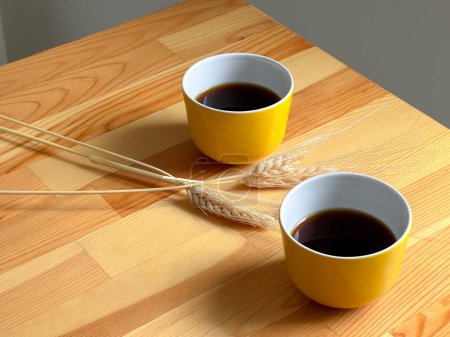 Foto de Un par de tazas estéticas amarillas de café negro y espiguillas de trigo en el fondo de una mesa de madera. Vista superior - Imagen libre de derechos