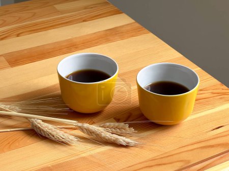 Foto de Dos tazas amarillas con café caliente en la mesa de madera. Junto a ti están las espigas de trigo - Imagen libre de derechos