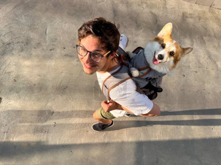 Foto de Sonriendo a los jóvenes y su adorable perro feliz viajando juntos, corgi en una mochila. - Imagen libre de derechos