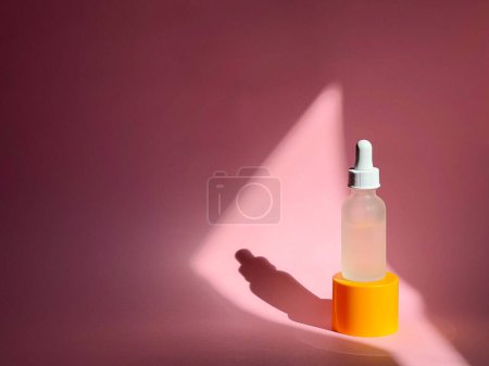 Foto de Suero en un frasco de cuentagotas de vidrio sobre un fondo rosa con una luz de sol sobre él. Cuidado de la piel. - Imagen libre de derechos
