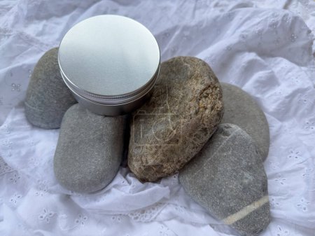 Foto de Vela en un frasco de metal redondo en color plata. Piedras y tela arrugada blanca como fondo - Imagen libre de derechos